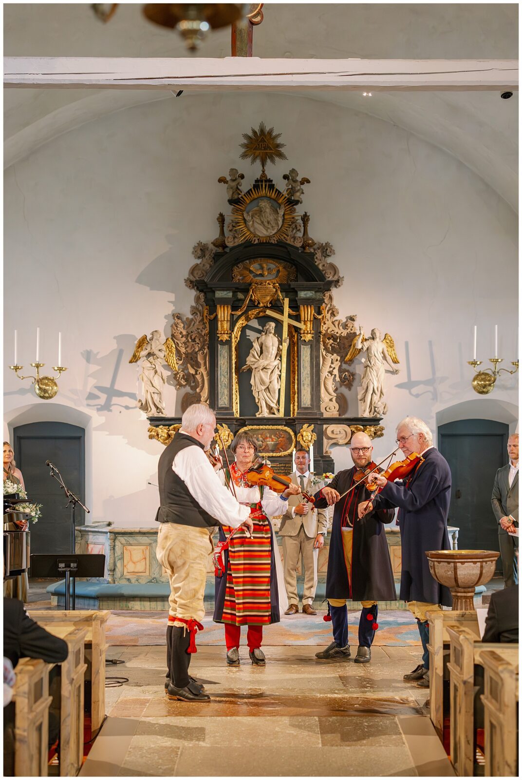 Folkmusiker spelar fiol framför altaret under vigseln i Rättviks kyrka, traditionell musik i fokus | Folk musicians performing with violins at the altar during the wedding ceremony in Rättvik Church