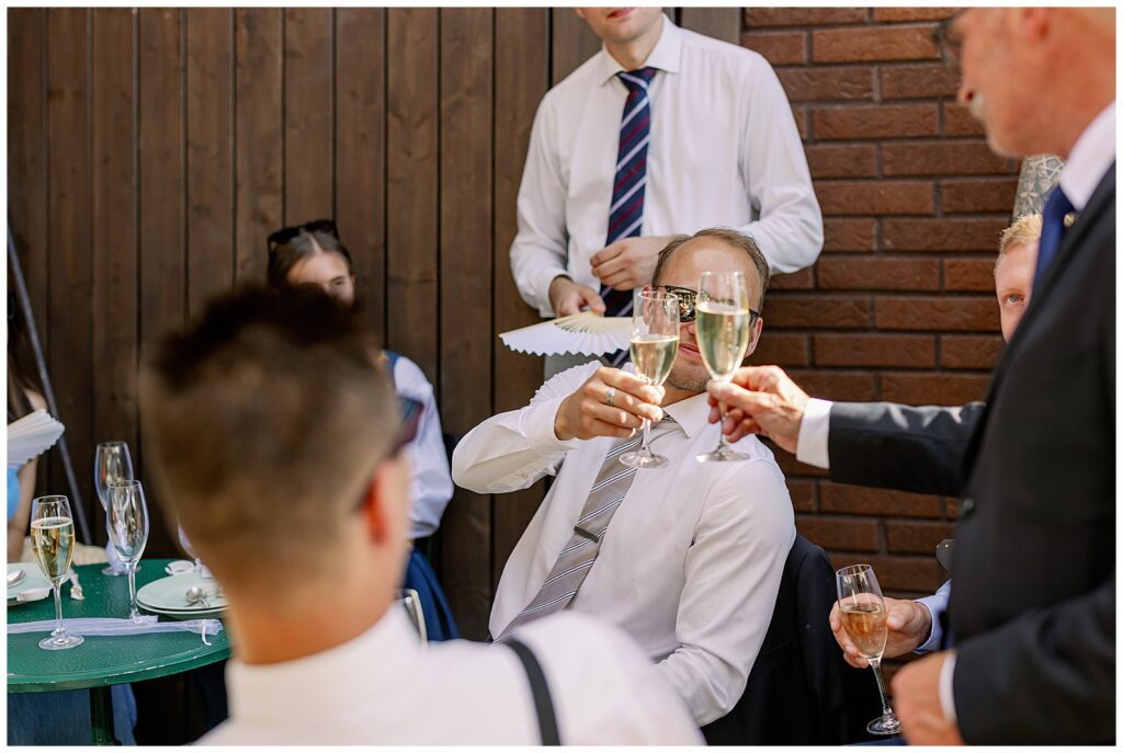 Bröllopsgäster skålar i champagne under bröllopsmingel på Green Hotel i Tällberg, Dalarna. / Wedding guests toasting with champagne during wedding mingling at Green Hotel in Tällberg, Dalarna.