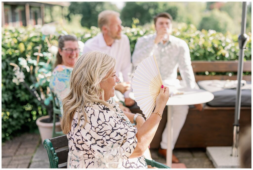 Gäst fläktar sig i sommarvärmen under bröllopsmingel på Green Hotel i Tällberg, Dalarna. / Guest cooling off in the summer heat during wedding mingling at Green Hotel in Tällberg, Dalarna.