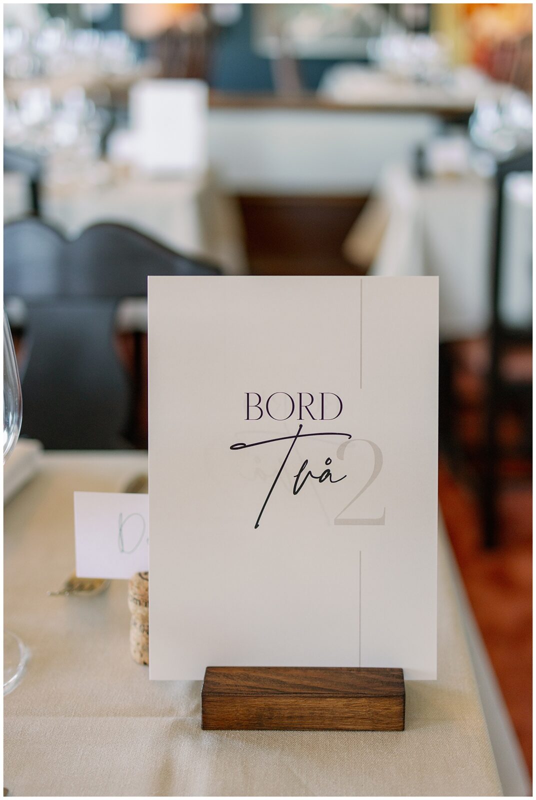 Bordsskylt med texten ”Bord två” placerad på dukat bröllopsbord under middagen på Green Hotel i Tällberg, Dalarna. / Table number sign reading “Table two” placed on a set wedding table during the reception at Green Hotel in Tällberg, Dalarna.