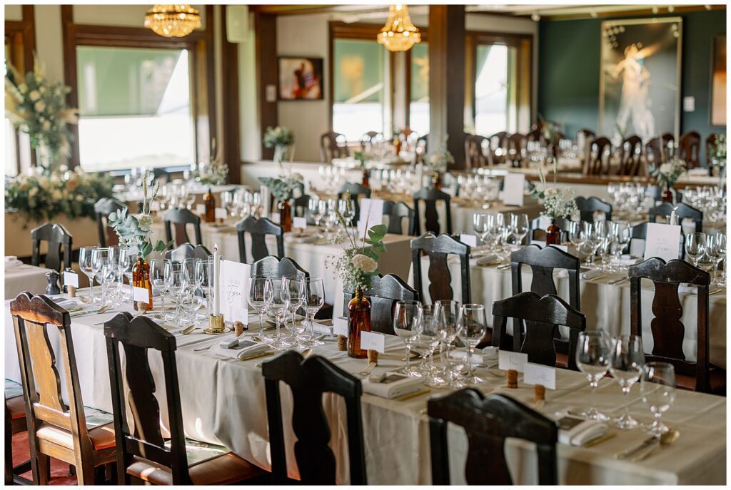 Långbord dukat för bröllopsmiddag med blommor och ljuskronor i matsalen på Green Hotel i Tällberg, Dalarna. / Long tables set for a wedding dinner with floral arrangements and chandeliers in the dining room at Green Hotel in Tällberg, Dalarna.