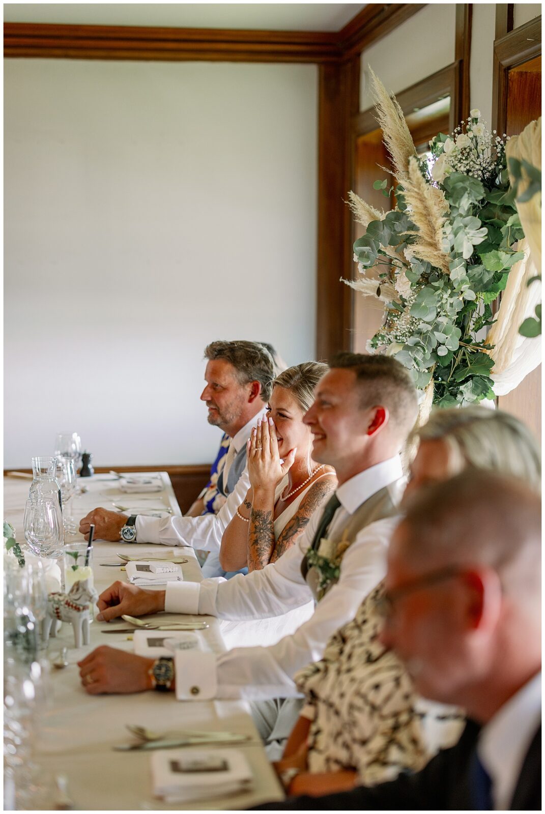 Brudpar sitter vid honnörsbordet och reagerar på tal under middagen på Green Hotel i Tällberg. / Bride and groom seated at the head table reacting to speeches during the dinner at Green Hotel in Tällberg.