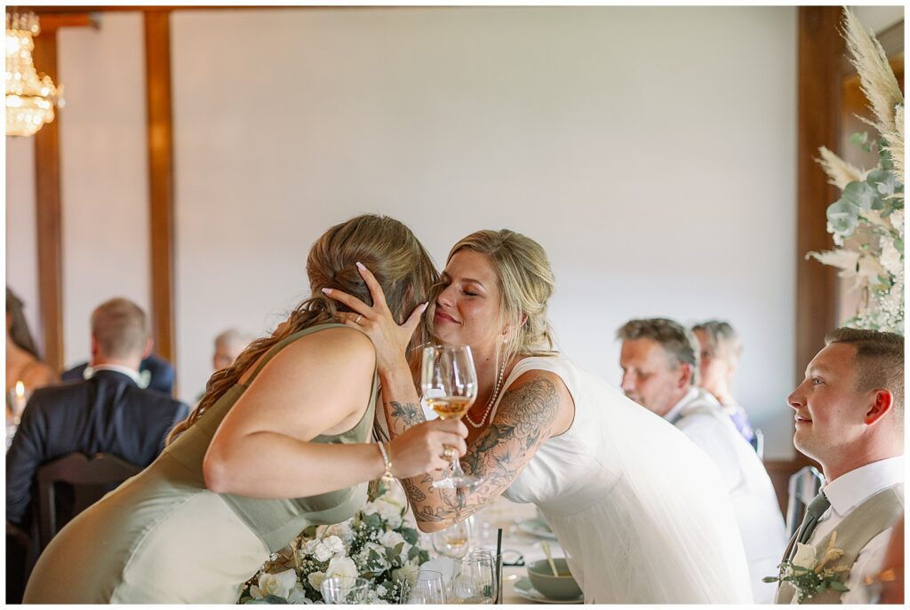 Bruden lutar sig fram och kramar en gäst vid middagsbordet under bröllopsfesten på Green Hotel i Tällberg, Dalarna. The bride leans forward to hug a guest at the dinner table during the wedding reception at Green Hotel in Tällberg, Dalarna.